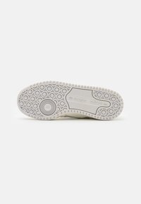 Biała podeszwa sportowego obuwia z okrągłym wzorem tekstury, z rowkami i wyraźnym logo Adidas. Wytrzymały materiał gumowy.