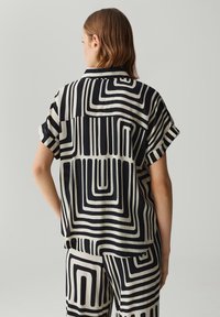 Kurzärmelige Bluse aus leichtem Stoff mit einem auffälligen schwarz-weißen geometrischen Muster, das sich durch unterschiedliche Linienstärken auszeichnet, und einem lässigen Schnitt.