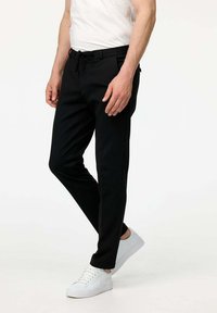 Pantaloni neri con vita a cordino, vestibilità slim e tasche laterali, abbinati a sneakers bianche. Tessuto morbido con un design classico.