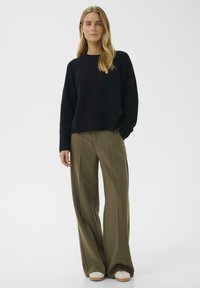Granatowy sweter w prążki, luźny krój, w połączeniu z oliwkowymi spodniami typu wide-leg i kremowymi sneakersami, ukazujący teksturowany materiał i prosty design.