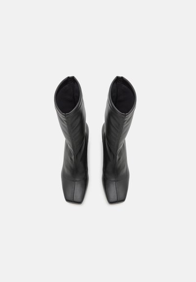 Botine negre din piele cu un finisaj neted, design cu vârful pătrat și fustă ajustată, având detalii cu cusături pe laterale.