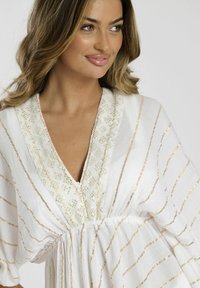 Blusa blanca con rayas doradas, con escote en V y detalles de encaje decorado. Tejido suelto y fluido con acentos texturizados.