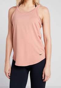 Débardeur de sport rose clair en tissu respirant, avec un col rond et un logo Nike noir sur le côté inférieur gauche.