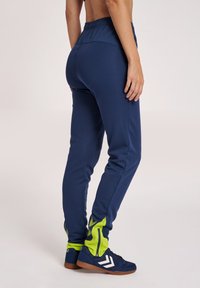 Marina atletiska byxor med en figurnära design, elastisk midja och neongröna detaljer. Dragkedja i nederkanten och en texturerad tygkvalitet ökar funktionaliteten.