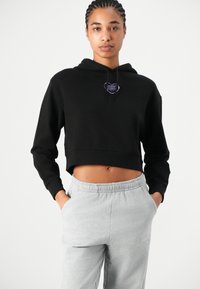 Cropped zwarte hoodie met een paarse hartlogo, gecombineerd met lichtgrijze sweatpants met een geborduurd accent en een elastische taille.