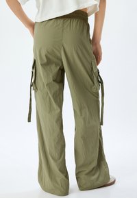 Olivgrüne Cargo-Hosen mit lockerer Passform, elastischem Bund, Seitentaschen und verstellbaren Bindebändern am Saum. Äußerst leichtes und strukturiertes Material.