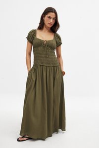 Olivenfarbenes Maxikleid mit Puffärmeln, gerafftem Mieder, Bindeband und Seitentaschen. Fließender Stoff mit strukturierter Oberfläche.