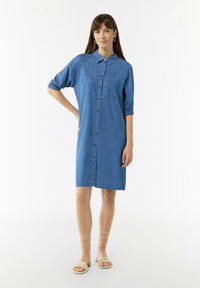 Sukienka koszulowa z denimu w jasnoniebieskim kolorze, zapinana na guziki, z krótkimi bufkami i dwoma kieszeniami na piersi. Luźny krój, sięgająca do kolan.
