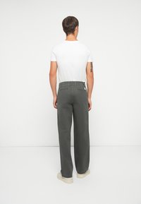 Men’s grey wide-leg trousers made of cotton, with two back pockets and a label on the waistband, paired with a white short-sleeve shirt.
