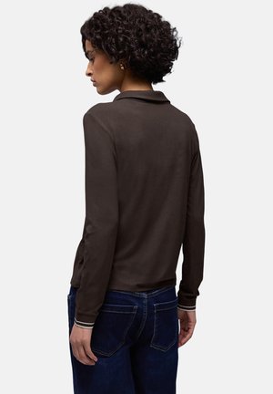 Haut marron à manches longues avec un col, présentant une texture lisse et des poignets rayés contrastés. Porté avec un pantalon en denim foncé. Design simple.