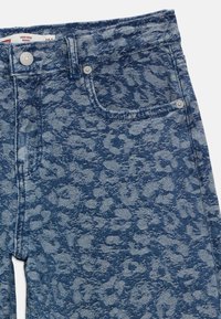 Jeans de ganga com corte baggy de cintura alta e padrão de leopardo azul, apresentando detalhes de botão frontal e rebites nos bolsos.