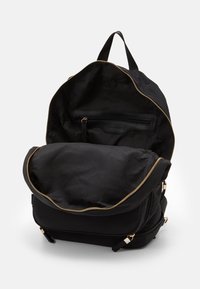 Svart ryggsäck med öppet toppfack som visar innersidans ficka med dragkedja och textilfoder, uppställd mot en enfärgad vit bakgrund.