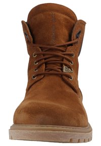 Bota de tornozelo em camurça castanha com biqueira arredondada, ilhós metálicos e atacadores grossos. Apresenta uma sola de borracha durável e uma marcação em relevo na língua.