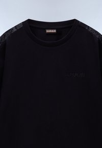 Černé bavlněné tričko s kulatým výstřihem, které má texturované černé akcenty na ramenou a embosované logo na přední straně.