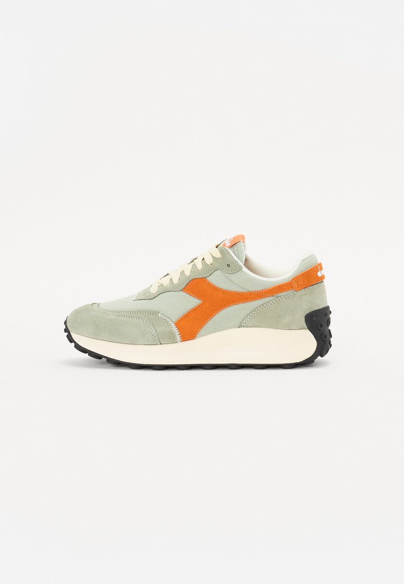 Light green suede sneakers with orange accents, textured materials, cream laces, and black rubber soles. Narrow design with logo detail.