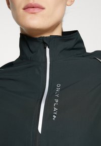 Chaqueta deportiva negra con un alto cuello, cremallera delantera, acentos reflectantes y el logo "ONLY PLAY" impreso en blanco. Material suave y ligero.