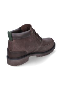 Botín de piel marrón con cuello acolchado, parte delantera con cordones, suela robusta y tirador verde en la parte trasera, inclinado para mostrar el lado exterior y la parte trasera.