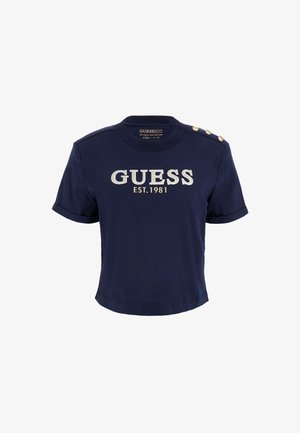 Tumed t-särk, mis on valmistatud 95% orgaanilisest puuvillast, millel on valge kiri "GUESS EST.1981" ja kuldsed nööbid õlal.