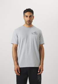 T-shirt en coton gris avec des manches courtes et un col rond, présentant une impression graphique d'un véhicule et du texte à l'avant.