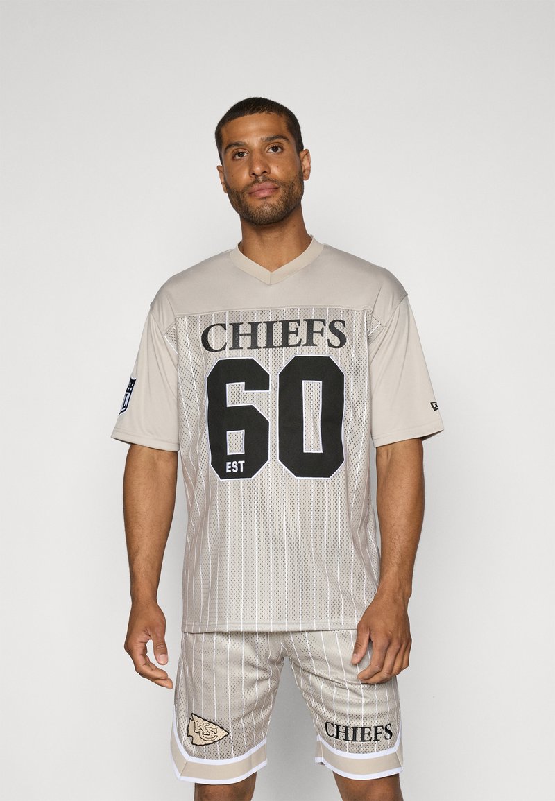 Μπεζ πλέγμα φανέλα ποδοσφαίρου με μαύρο κείμενο "CHIEFS" και αριθμό "60", σε συνδυασμό με ταιριαστές βερμούδες με λευκές λεπτομέρειες και λογότυπο.