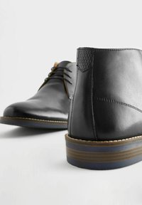 Zapatos de cuero negro con un acabado suave, punta redonda y diseño de cordones. Acento texturizado notable en el talón y detalle de suela a rayas.