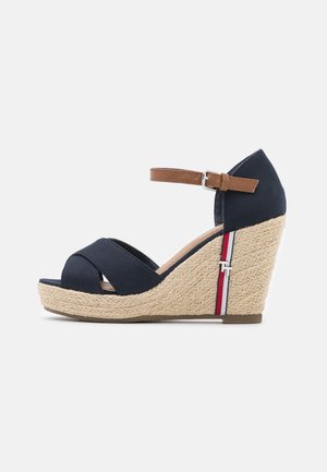 Marineblå kilehæl sandal med tan ankelrem, vævet beige platformhæl og rød-hvid-blå stribe detalje på siden.