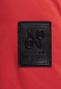 Rød stoff med en teksturert svart lærflekke. Flekken har det pregete logoet "N" og "NAVAHOO EST 2014" med en glatt overflate.