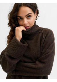 Maglione a collo alto di colore marrone scuro, lavorato a maglia, con polsini a costina. Fit rilassato con spalle scese e una finitura morbida e testurizzata.