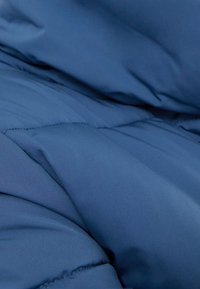Close-up of soft, wrinkled blue fabric, likely part of a quilted blanket or padded jacket with visible stitching.