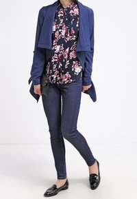 Navy open-front cardigan over a floral blouse, dark skinny jeans, and black loafers. Features floral print, smooth fabric, and structured design.