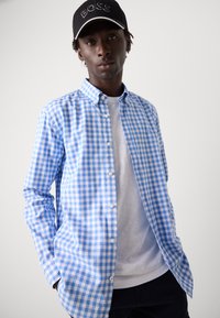 Blå og hvit gingham rutete skjorte med knapp-ned krage, bomullsstoff, lange ermer, brukt over en hvit T-skjorte, lagdelt stil.