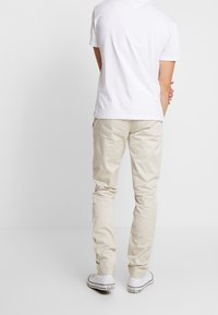 Beige bomullschinos med slim fit, som har sidfickor och en mjuk yta. Bärs med en enkel vit T-shirt och vita sneakers.
