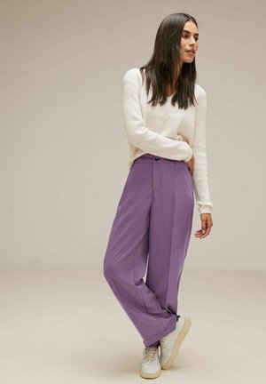 Pantaloni larghi viola realizzati in tessuto leggero, con chiusura anteriore a bottoni e tasche laterali, abbinati a un maglione lavorato a maglia bianco.
