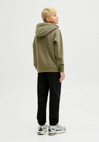 Felpa con cappuccio verde oliva, abbinata a pantaloni della tuta neri con polsini elasticizzati. Calzature comprendono sneaker grigie e bianche.
