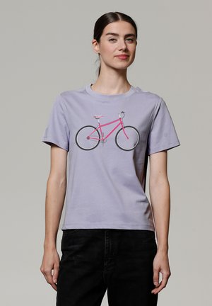 T-shirt en coton lilas clair avec un motif de vélo rose, manches courtes et col rond. La coupe est décontractée et sans structure.