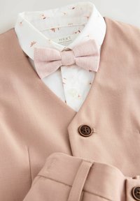 Gilet rose clair avec une finition texturée, associé à une chemise blanche ornée de motifs floraux, et une cravate nœud rose. Détail de bouton marron inclus.