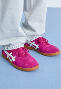 Zapatillas de ante rosa con detalles en blanco, con un diseño de bajo perfil, puntera redonda y suela de goma. Combinadas con unos vaqueros de denim gris claro.