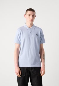 Polo bleu clair en coton, avec un col, des manches courtes et une petite étiquette de logo sur la poitrine.