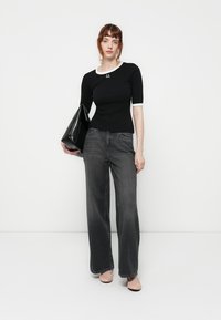Black fitted top with white collar and detailing, wide-leg gray jeans, and a large black handbag. Smooth fabric and relaxed silhouette.