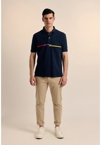 Polo de algodón en color navy con mangas cortas, cuello tipo polo y una franja horizontal rosa y amarilla en el pecho.