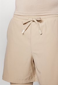 Beige lühikesed püksid elastse vöökoha ja sidumisnööriga, sujuva tekstuuri ja lohaka sobivusega, ideaalne igapäevaseks kandmiseks.