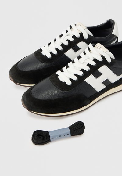 Baskets noires et grises avec une tige en cuir texturé, des accents en daim, des lacets blancs et un logo blanc bien en évidence. Comprend un lacet supplémentaire noir.