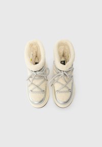 Cremefarvede, pelsede støvler med sølvfarvede detaljer, grå snørebånd og en kraftig sål. Har en høj, polstret krave for komfort.