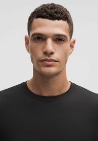 Fekete, rövid ujjú póló, kerek nyakkivágással. Simogatós, testhezálló anyag, minimális varrásokkal, amely tiszta, modern dizájnt mutat.