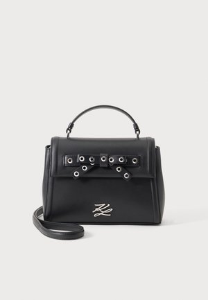 Sac à main en cuir noir avec poignée supérieure, bandoulière amovible, détail nœud œillet argenté sur le rabat et emblème logo argenté sur le devant.