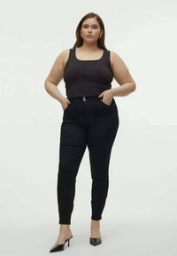 Black high-waisted pants with a smooth texture, featuring a zip closure and two front pockets, paired with a fitted black tank top.