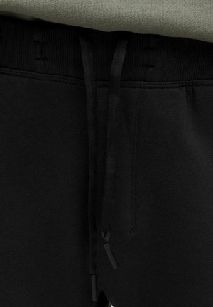 Mustad mustad püksid, millel on nööriga vöökoht, on kihitatud ning pealt kumab läbi roheline dressipluus.