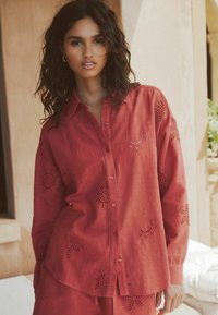 Punane linane särk, millel on liblika- ja lillelõike mustrid, esiosa kinnitatav nööpidega, pikad varrukad ja mugav lõige.