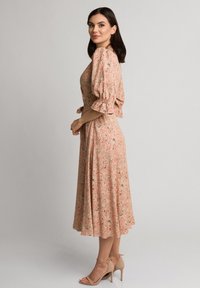 Sukienka midi w kwiatowy wzór w odcieniach brzoskwini, z bufiastymi rękawami i dopasowanym talią. Dopełniona cielistymi sandałami na obcasie. Gładka tekstura materiału.