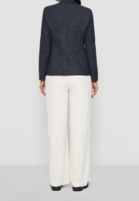 Navyblå strukturerad kavaj med skräddarsydd passform och mjuka slag, kombinerad med krämfärgade vida byxor, som visar upp en minimalistisk design.